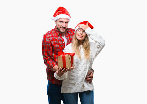 Young couple in love wearing christmas hat and holding present over isolated background stressed with hand on head, shocked with shame and surprise face, angry and frustrated. Fear 