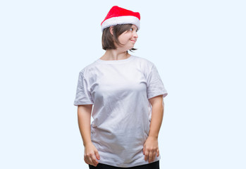 Young adult woman with down syndrome wearing christmas hat over isolated background looking away to side with smile on face, natural expression. Laughing confident.