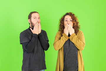 Young couple over green background, afraid and terrified with fear expression, shouting in shock. Panic concept.