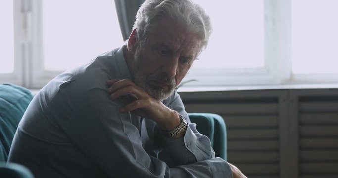 Upset senior man sitting alone at home feeling sad worried