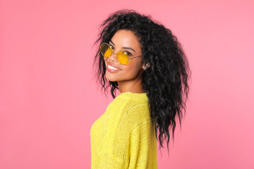 Sweet youth. Gorgeous African ethnic girl in a yellow sweater and yellow glasses is posing in profile, her head turned to the camera, smiling broadly.