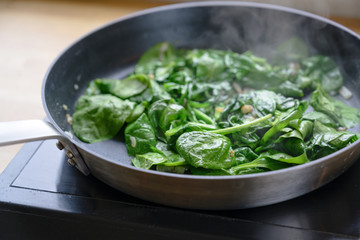 fried spinach leaves in a pan on the stove, healthy cooking concept