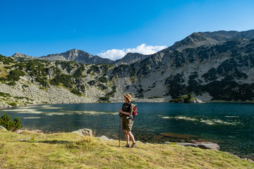 Fototapeta na wymiar Young woman with backpack hiking in the mountains near beautiful lake 