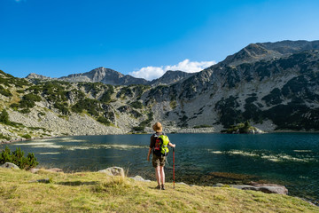 Young woman with backpack hiking in the mountains near beautiful lake 
