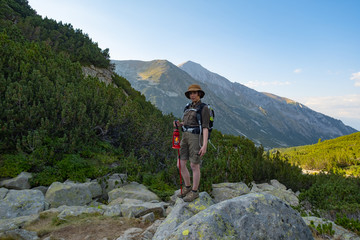 Young happy female with backpack and gas lantern stand in the beautiful mountains