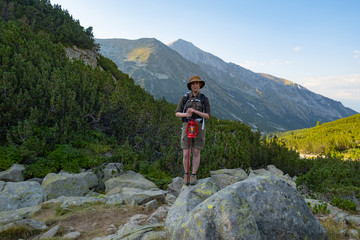 Young happy female with backpack and gas lantern stand in the beautiful mountains