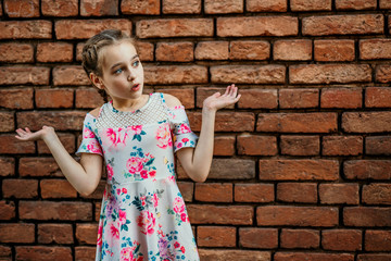 teenager girl spreads her arms to the side, emotion of surprise on a background of a brick wall