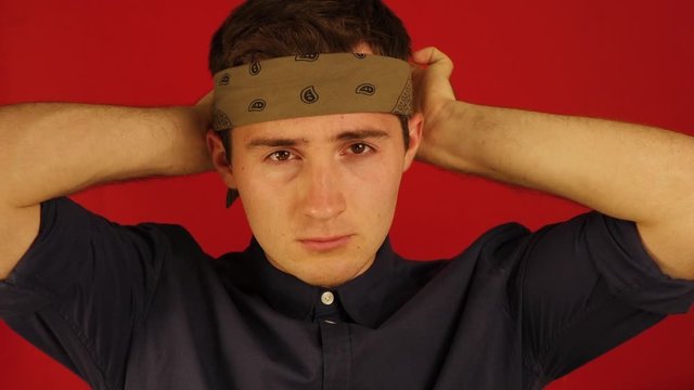 a young guy puts a bandana on his head on an isolated red background
