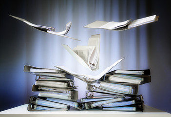 flying ring binders with files and documents are landing on stacks on an office desk, concept of...