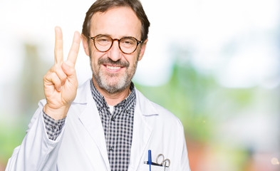 Middle age doctor men wearing medical coat showing and pointing up with fingers number two while smiling confident and happy.