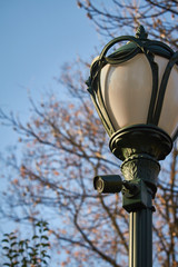 Vintage lantern with a surveillance camera in a public park in autumn in front of a blue sky, selective focus