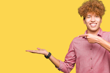 Young handsome business man with afro hair amazed and smiling to the camera while presenting with hand and pointing with finger.