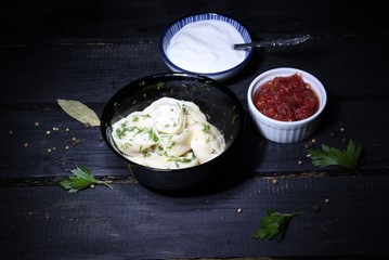 Cooked boile dumplings in pot with sauces and spices on wooden black background