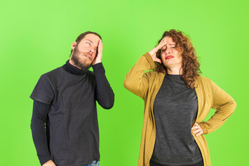 Young beautiful couple together over green background with hand on head for pain. Suffering migraine.