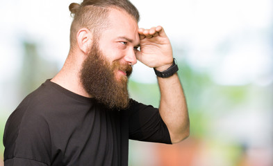Young blond man wearing casual t-shirt very happy and smiling looking far away with hand over head. Searching concept.