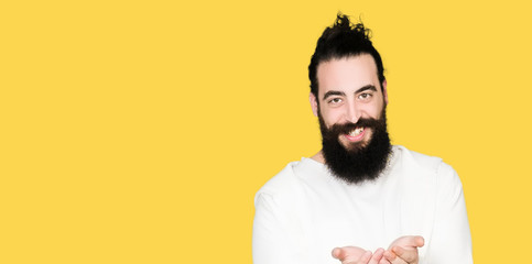 Young hipster man with long hair and beard wearing sporty sweatshirt Smiling with hands palms together receiving or giving gesture. Hold and protection