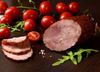 Dried smoked sausage with tomato on a dark brown plate