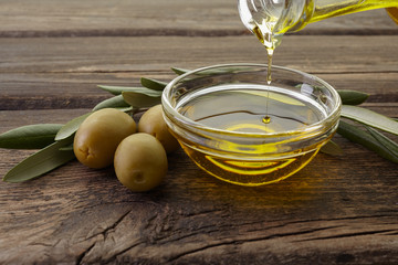 Bottle pouring olive oil in a bowl on vintage wooden background