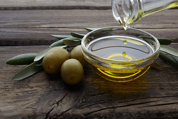 Bottle pouring olive oil in a bowl on vintage wooden background