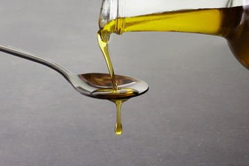 pouring olive oil from glass bottle on grey background