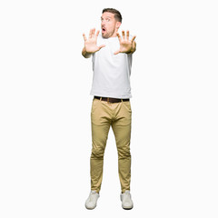 Handsome man wearing casual white t-shirt afraid and terrified with fear expression stop gesture...