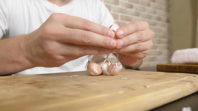 a man peels garlic sitting at a table on a background of a brick wall.