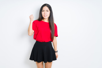 Beautiful brunette woman wearing red t-shirt and skirt over isolated background angry and mad raising fist frustrated and furious while shouting with anger. Rage and aggressive concept.