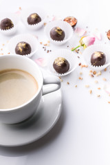 White ceramic cup of coffee and chocolate candies with handmade nuts on a white background. Vertical shot