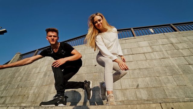 Modern dancers in the street. Urban lifestyle. Hip-hop generation. Boy's and girl's emotional moves on the video. Young couple at stone wall background is looking into the camera.