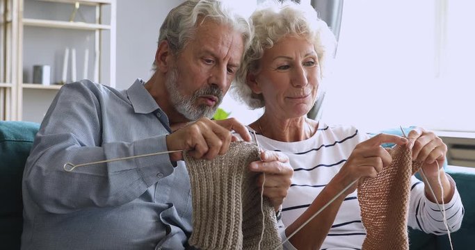 Elderly grandfather learning knitting helping older wife at home
