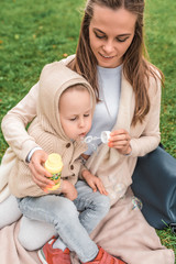 Soap bubbles are launched. Happy people play laughing and having fun positive emotions, in warm clothes in fall, in sweater with hood. Mom woman with a little boy son of 4-5 years old, lie on grass.