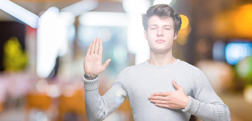 Young handsome man wearing winter sweater over isolated background Swearing with hand on chest and...
