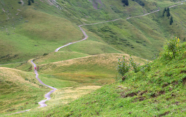 Curvy mountain road crossing the Alps in diagonal with a hiking man in red jacket