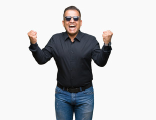 Middle age arab man wearing sunglasses over isolated background celebrating surprised and amazed for success with arms raised and open eyes. Winner concept.