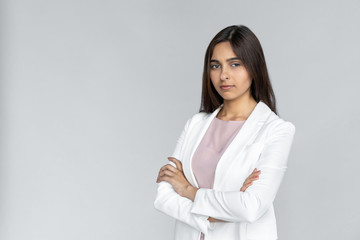 Serious young adult indian businesswoman in white formal wear crossed arm on chest and looking at...