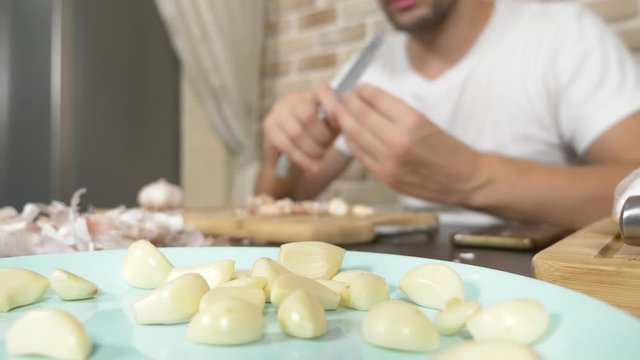a man peels garlic sitting at a table on a background of a brick wall.