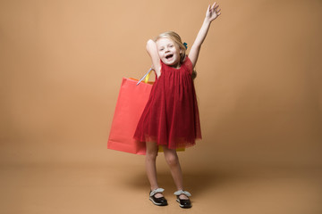 A young girl in a red dress and with shopping bags, very happy shopping. A young girl stands on an orange background