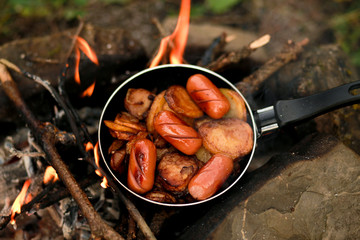 Breakfast of fried eggs and sausages in a pan. Kitchen for camping: chicken egg with a bright yolk in a cast-iron skillet near a campfire close-up, breakfast on an open fire.Camping food making.