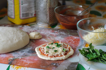 Process of cooking little pizza at home. Flour, dough, parsley, tomato sauce, cheese and  steel grinder around it