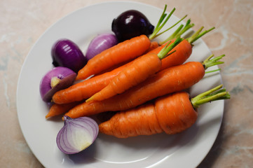 Fresh wet organic carrots with red onion on a white plate