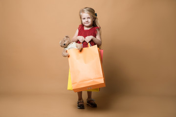 A young girl in a red dress and with shopping bags, very happy shopping. A young girl stands on an orange background