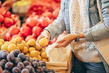 Female hands puts fruits and vegetables in cotton produce bag at food market. Reusable eco bag for shopping. Sustainable lifestyle. Eco friendly concept.