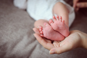 Mother's hand holding tiny newborn's feet closeup