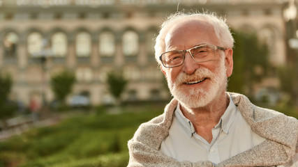 It’s never too late. Portrait of happy and handsome bearded senior man in glasses looking at camera and smiling while spending time outdoors on a sunny day