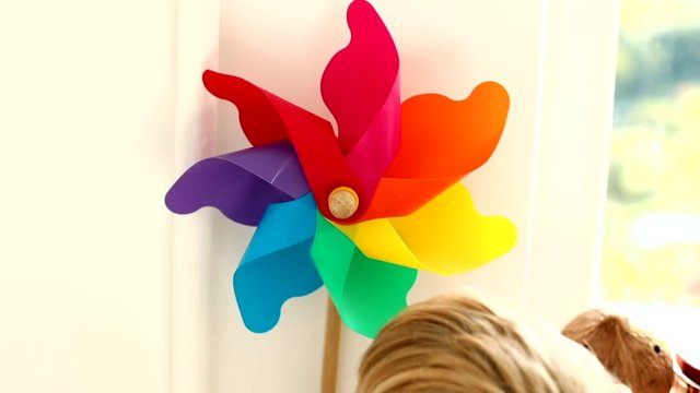 Little blonde caucasian baby boy playing with rainbow windmill flower toy in beautiful summer sunny day at home with modern stylish interior on background. Cute smiling happy male child.