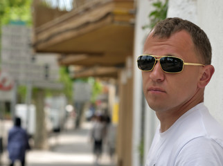 Portrait of a young man on a sunny day near the wall on a street background, looking at the camera