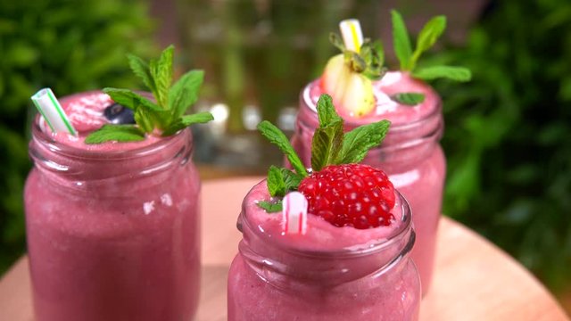 Healthy berries smoothie in glasses rotating on plate. Fresh strawberries, blueberries and raspberries, mint leaves and plastic sticks. Milkshakes for refreshment, healthy breakfast. Nourishing