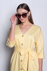 Fashion model in big sunglasses wearing yellow dress with buttons posing over gray background