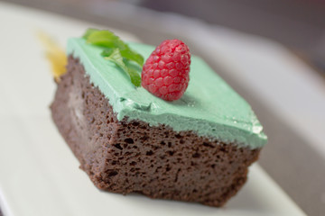 Decadent vegan chocolate cake topped with vibrant mint frosting and a fresh raspberry, captured in a bright, upscale close-up.