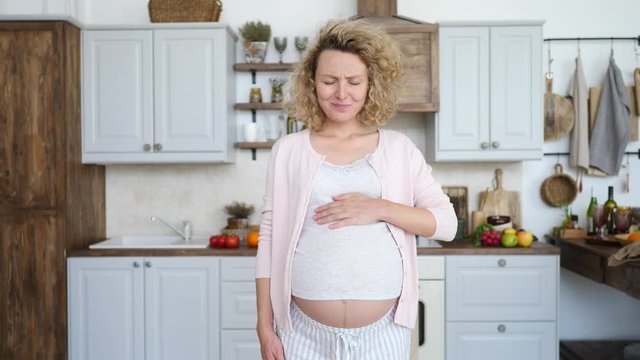 Pregnant Woman Suffering From Heart Burn In Kitchen At Home.